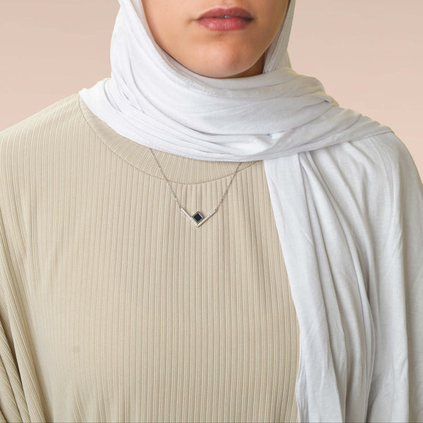 Model wearing a silver necklace with an intertwined pendant containing a square black nano chip with the full Quran, photographed against a beige-toned background.