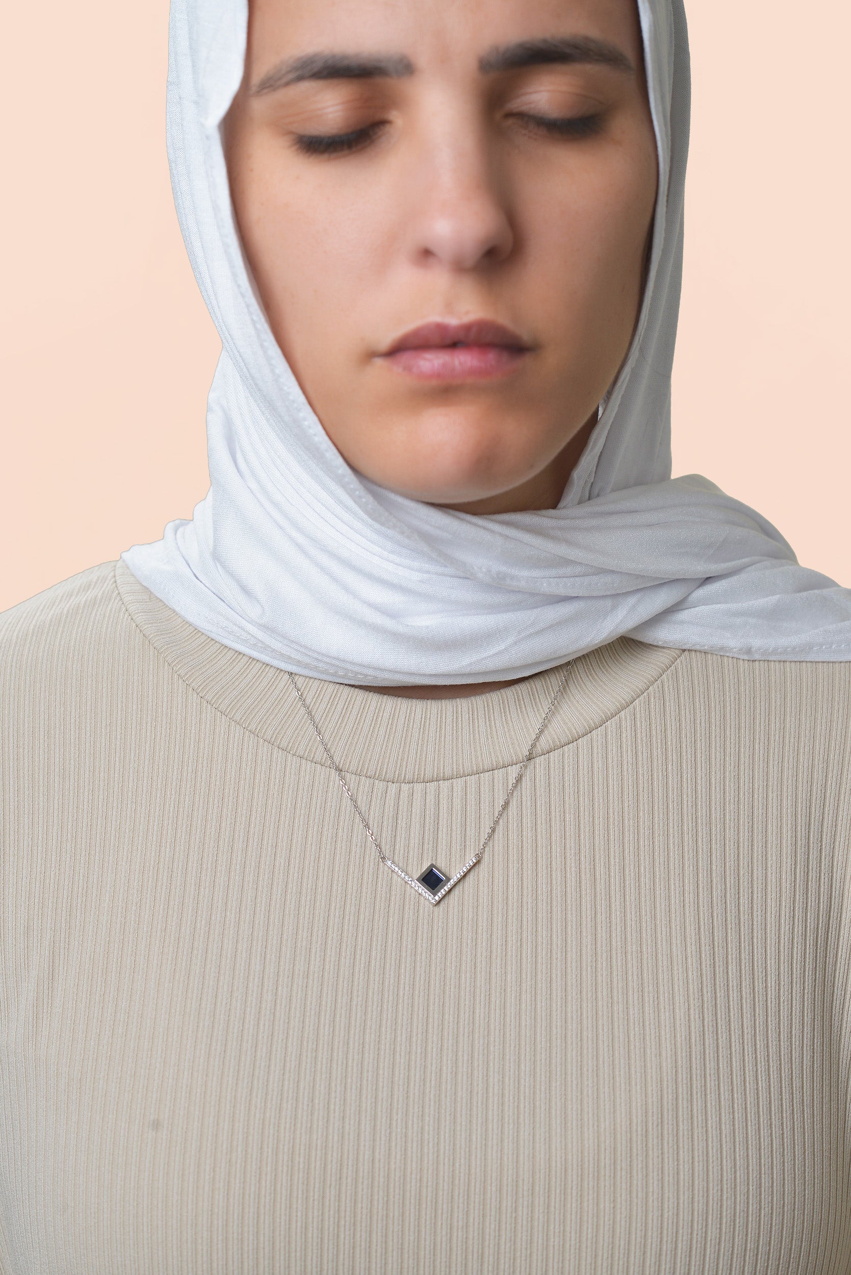 Model wearing a silver necklace with an intertwined pendant containing a square black nano chip with the full Quran, photographed against a beige-toned background.