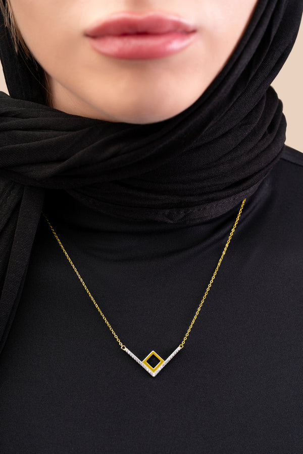 Model wearing a gold necklace with an intertwined pendant containing a square black nano chip with the full Quran, photographed against a beige-toned background.