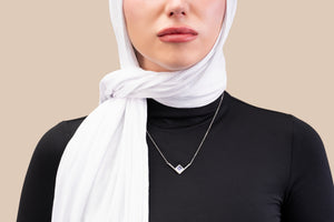 Model wearing a silver necklace with an intertwined pendant containing a square black nano chip with the full Quran, photographed against a beige-toned background.