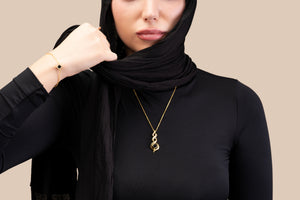 Model wearing a gold bracelet featuring a square black nano-chip charm that contains the full Quran, photographed against a beige-toned background.