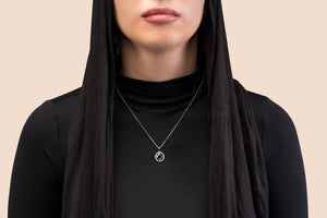 Model wearing a silver necklace with a round pendant that includes a black center stone and a nano chip micro-engraved with the entire Quran.