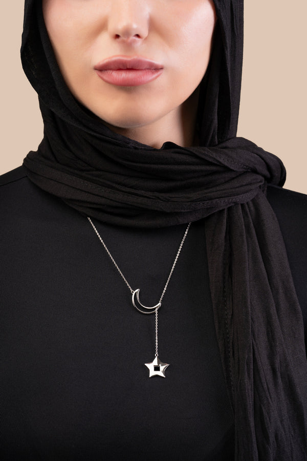 Model wearing a silver crescent-and-star necklace, with the star containing a black nano chip inscribed with the entire Quran, photographed against a beige-toned background.