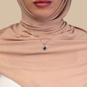 Model wearing a silver necklace with a round pendant that includes a black center stone and a nano chip micro-engraved with the entire Quran.