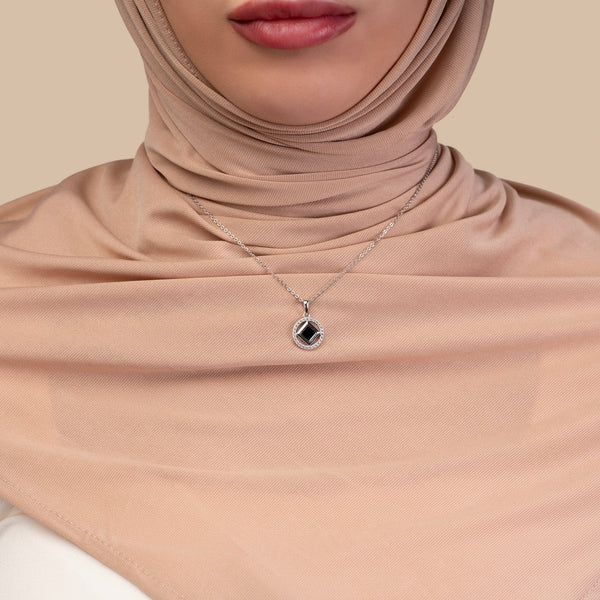 Model wearing a silver necklace with a round pendant that includes a black center stone and a nano chip micro-engraved with the entire Quran.