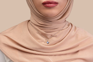 Model wearing a gold necklace with a square black nano-chip pendant that includes a Quran-inscribed nano chip, photographed against a soft beige-toned background.