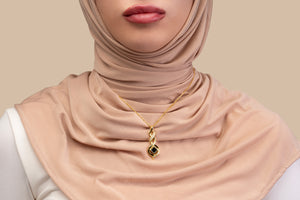 Model wearing a gold necklace with an intertwined pendant containing a square black nano chip with the full Quran, photographed against a beige-toned background.