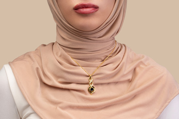 Model wearing a gold necklace with an intertwined pendant containing a square black nano chip with the full Quran, photographed against a beige-toned background.