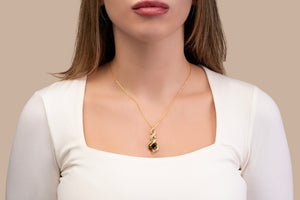 Model wearing a gold necklace with an intertwined pendant containing a square black nano chip with the full Quran, photographed against a beige-toned background.