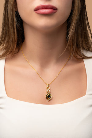 Model wearing a gold necklace with an intertwined pendant containing a square black nano chip with the full Quran, photographed against a beige-toned background.