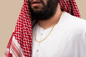 Male model wearing a gold Cuban chain necklace with a black nano chip near the clasp containing the full Quran, photographed against a beige-toned background.