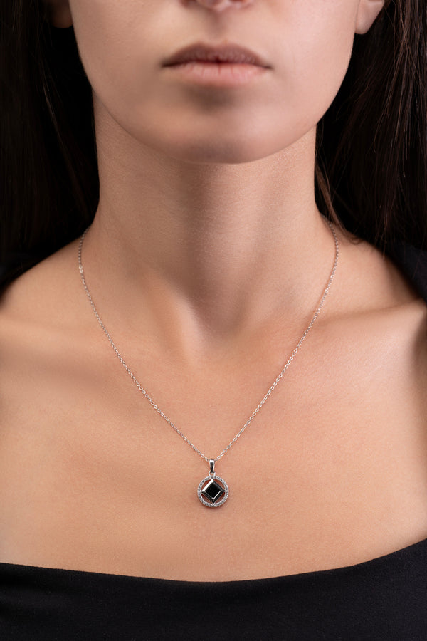 Model wearing a silver necklace with a round pendant that includes a black center stone and a nano chip micro-engraved with the entire Quran.