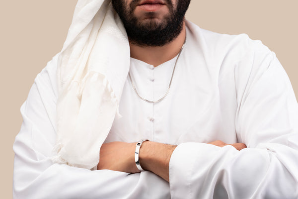 Male model wearing a silver Cuban chain necklace with a black nano chip near the clasp containing the full Quran, photographed against a beige-toned background.