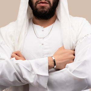 Male model wearing a silver cuff bracelet with a built-in black nano chip containing the full Quran, photographed against a beige-toned background.