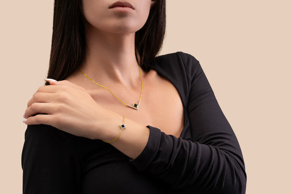 Model wearing a gold necklace with an intertwined pendant containing a square black nano chip with the full Quran, photographed against a beige-toned background.