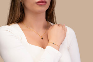 Model wearing a gold bracelet featuring a square black nano-chip charm that contains the full Quran, photographed against a beige-toned background.