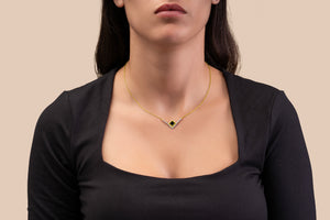 Model wearing a gold necklace with an intertwined pendant containing a square black nano chip with the full Quran, photographed against a beige-toned background.