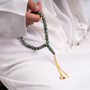 Close-up of a person holding a green gemstone tasbih with gold-plated tassels, featuring an embedded nano chip with the entire Quran.
