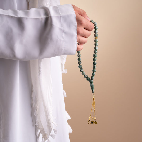 Close-up of a person holding a green gemstone tasbih with gold-plated tassels, featuring an embedded nano chip with the entire Quran.
