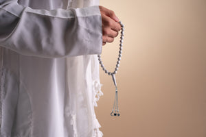 Model holding a silver tasbih with white stones and a silver pendant that includes a Quran-inscribed nano chip, photographed against a soft beige-toned background.