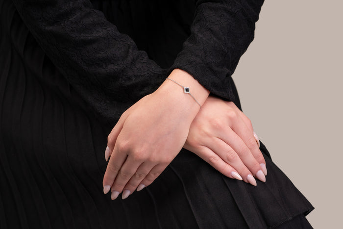 Model wearing a silver bracelet featuring a square black nano-chip charm that contains the full Quran, photographed against a beige-toned background.