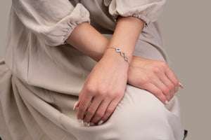 Model wearing a silver bracelet with an intertwined side design and a central square pendant that contains a black nano chip inscribed with the entire Quran, photographed against a beige-toned background.