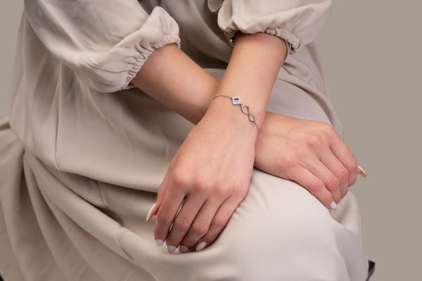 Model wearing a silver bracelet with an intertwined side design and a central square pendant that contains a black nano chip inscribed with the entire Quran, photographed against a beige-toned background.